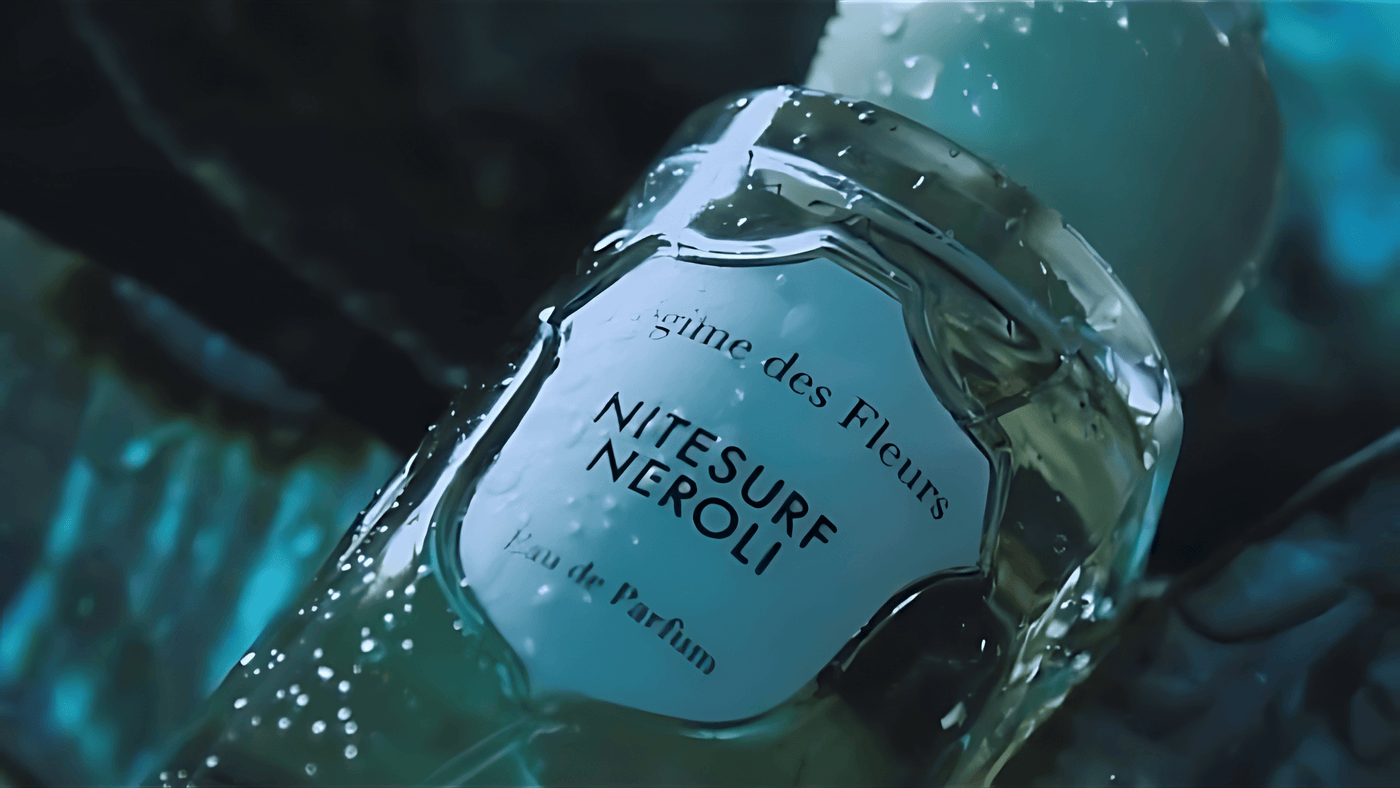Close up of Régime des Fleurs Nitesurf Neroli perfume bottle with droplets of water on it, in a blue tint.