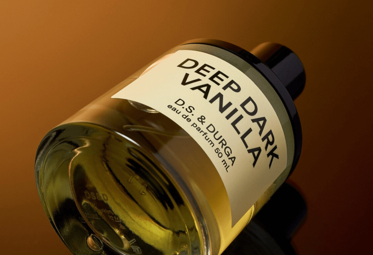Close-up of DS & Durga Deep Dark Vanilla perfume bottle on its side on an ombre brown background.