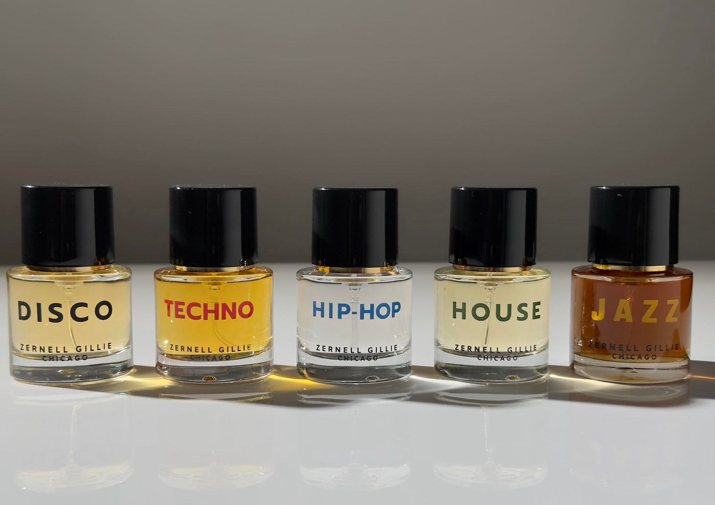 Five Zernell Gillie round clear glass perfume bottles, each with a music genre printed on them: Disco, Techno, Hip-Hop, House, Jazz.