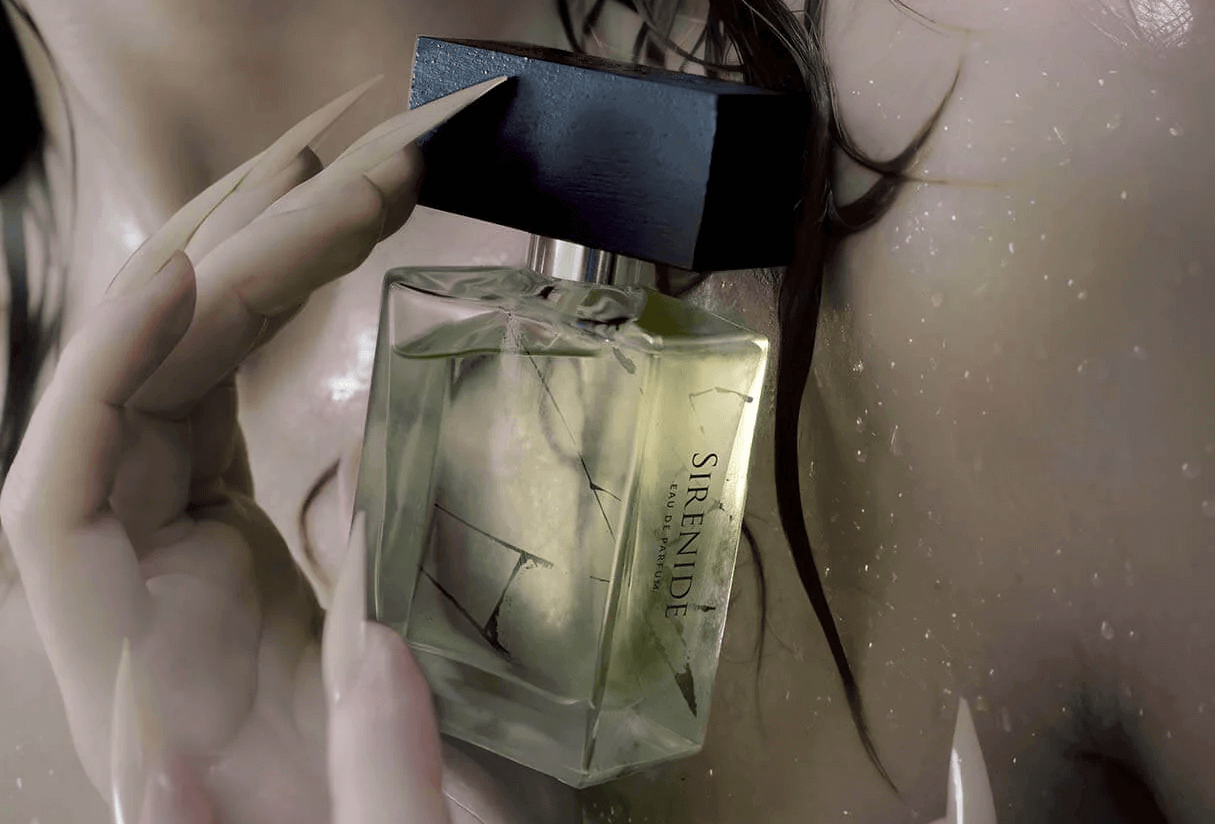 Close up of a woman's hands with long taupe fingernails, holding a bottle of Sirenide perfume in front of her chest, with drops of water on her skin.